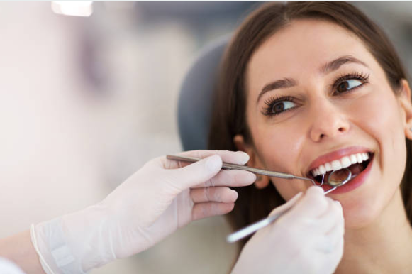 Woman patient in a dental chair having her teeth examined with a mirror and dental explorer by a gloved dentist.