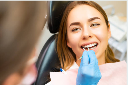 Dental patient in a chair receives dental care; clinician in blue gloves works on her teeth with a cheek retractor and tools nearby.